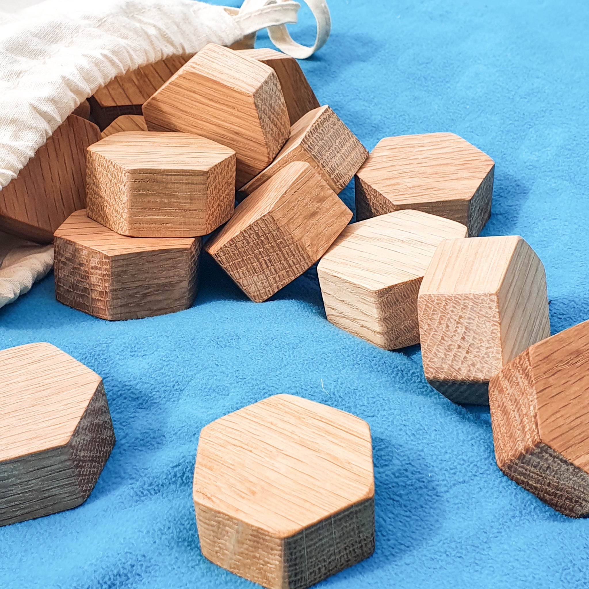 Wooden oak small hexagon blocks tipped out of a cotton bag onto a blue fleece playmat.