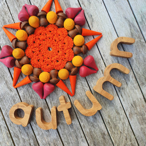 Open image in slideshow, handmade wooden oak alphabet letters toy used to spell the word autumn on a grey wooden background, next to a mandala created with red, orange, yellow and brown toys.
