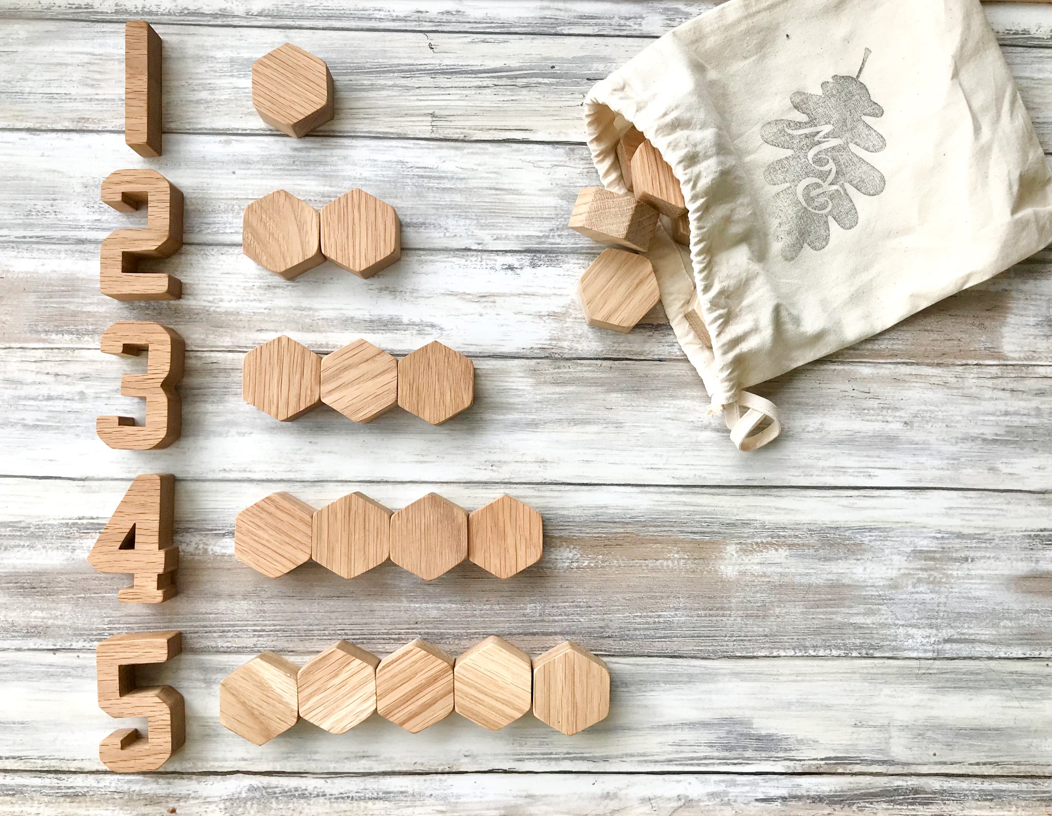 Wooden oak small hexagon blocks tipped out of a cotton bag onto a wooden floor. Wooden numbers arranged 1-5 with hex blocks next to each number with the corresponding amount