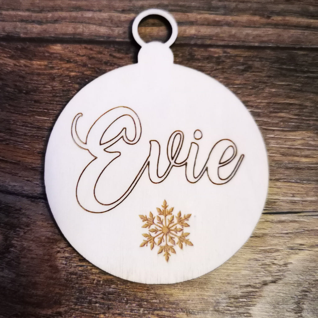 Wooden birch plywood lasered bauble shape with the name Evie in script and a snowflake on the bottom. on a wooden background