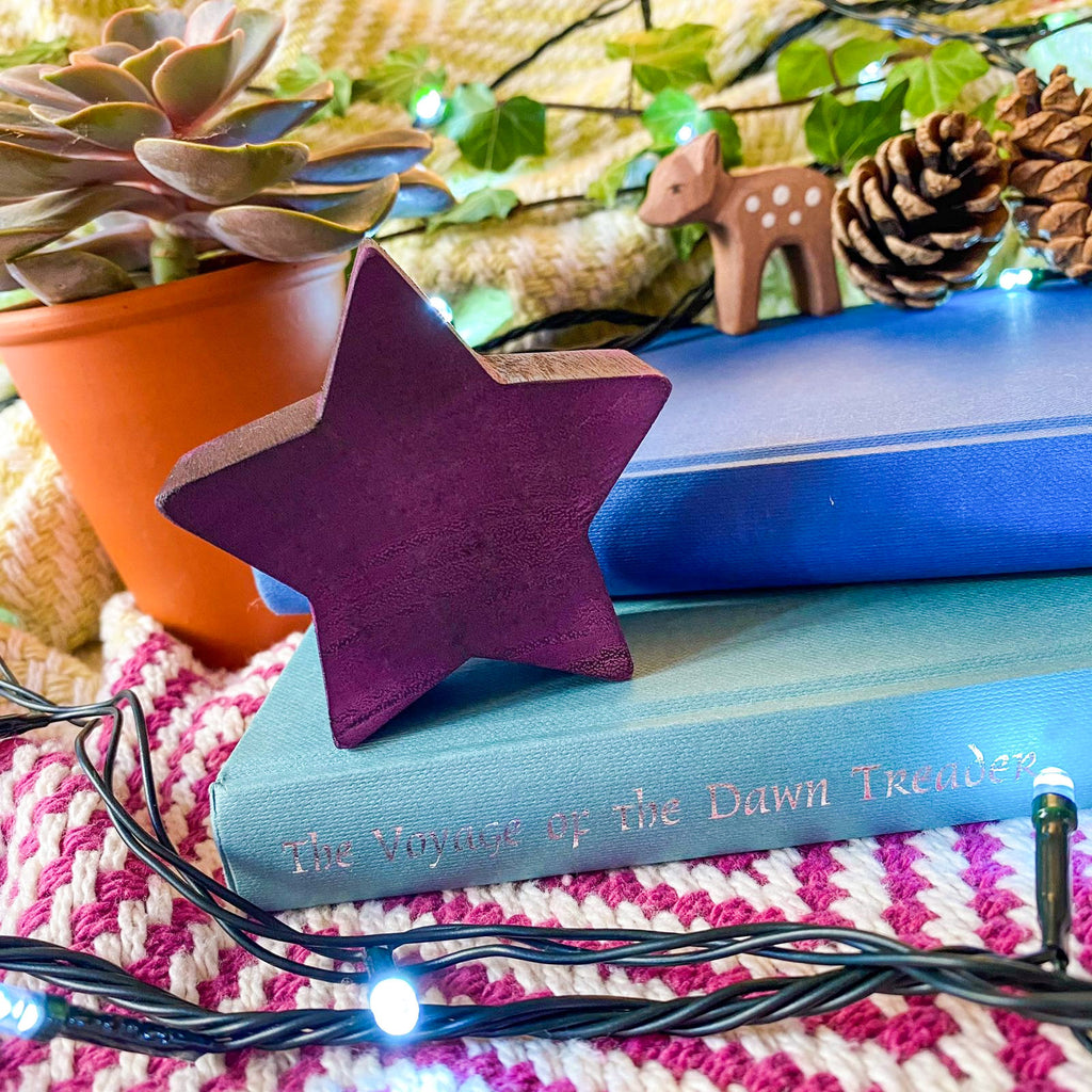 Wooden purpleheart star decor item. Stood on two books with fairy lights around and autumnal items. wooden fawn in the background 
