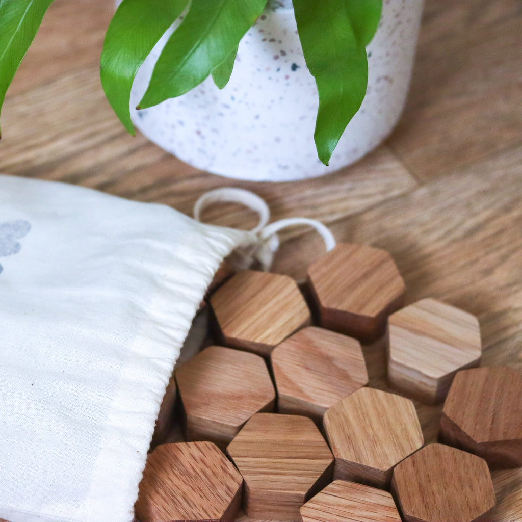 Wooden oak small hexagon blocks tipped out of a cotton bag onto a wooden floor with a plant in the background