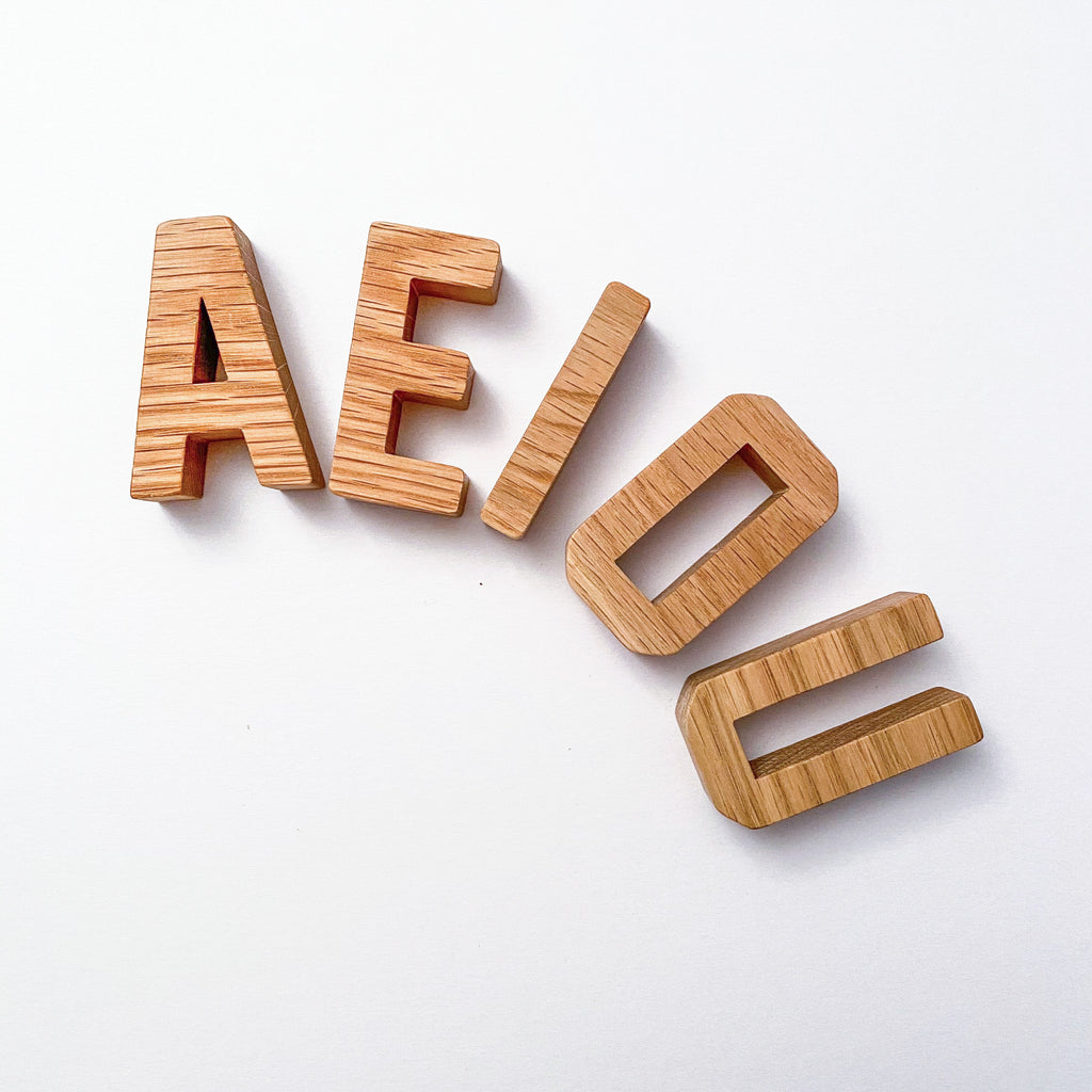 Wooden oak block capital letters AEIOU arranged in an arc on a white background
